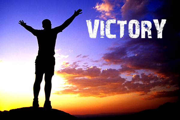 Man celebrating a victory at the top of a mountain with hands raised.